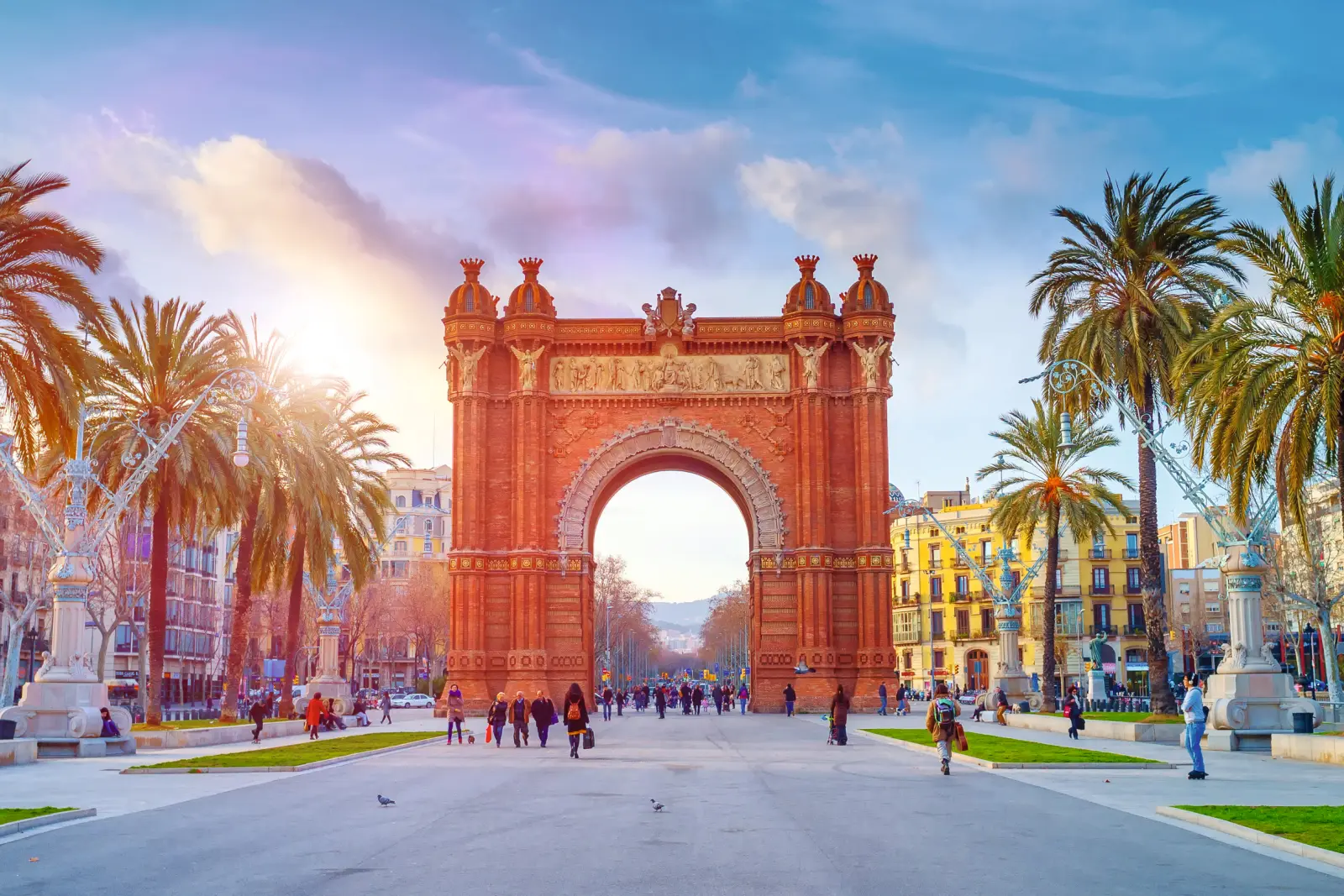 Triumphal arch in Barcelona on a sunny day, surrounded by people and palm trees.