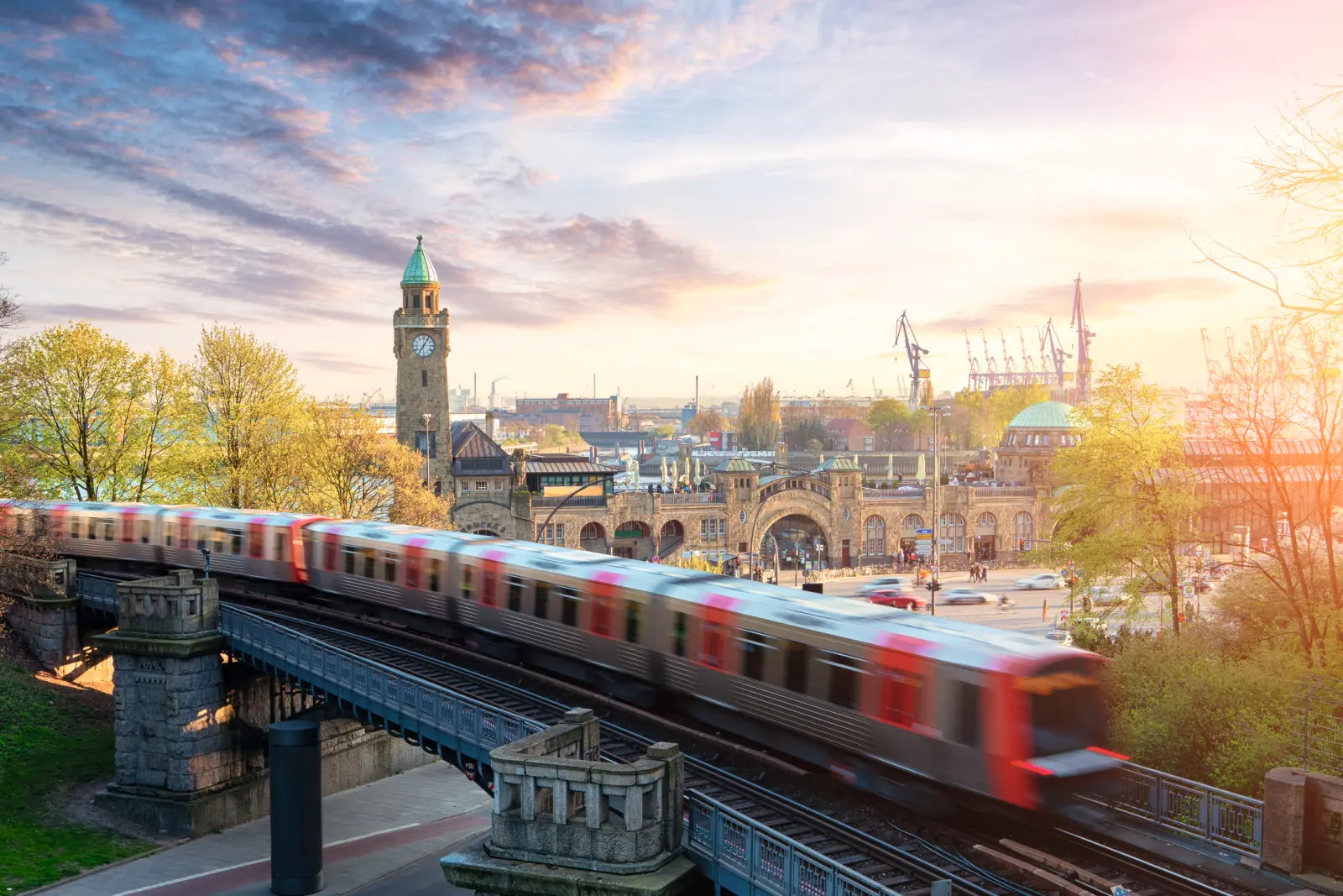 Treno su un ponte davanti al porto di Amburgo e a un edificio storico al tramonto.