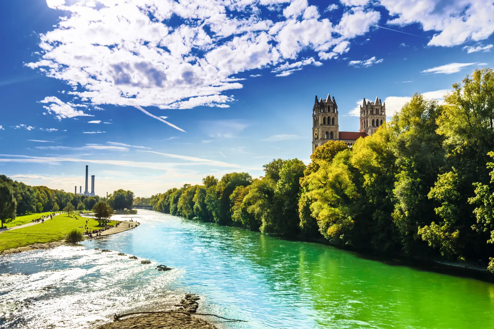 Rivière bordée d’arbres verts et cathédrale à l’arrière-plan sous un ciel bleu.