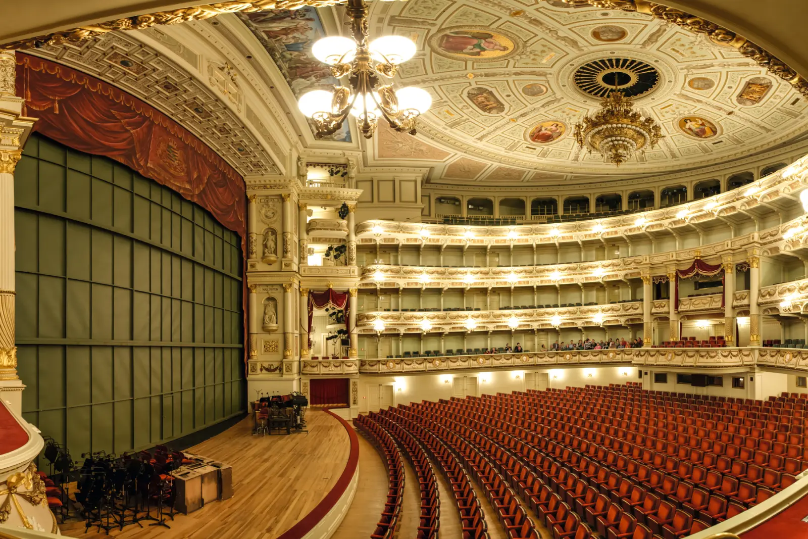 Interno di un sontuoso teatro con poltrone vuote e soffitto decorato.
