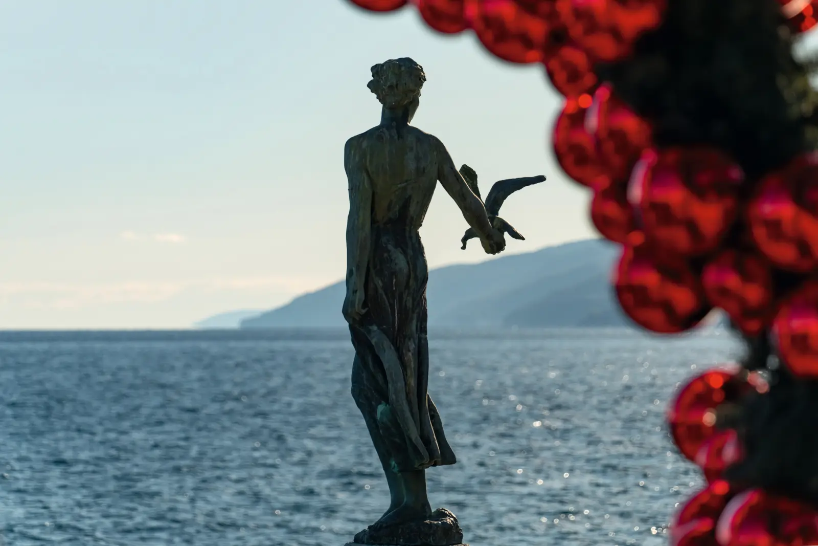 Statua sul mare con decorazioni rosse in primo piano.