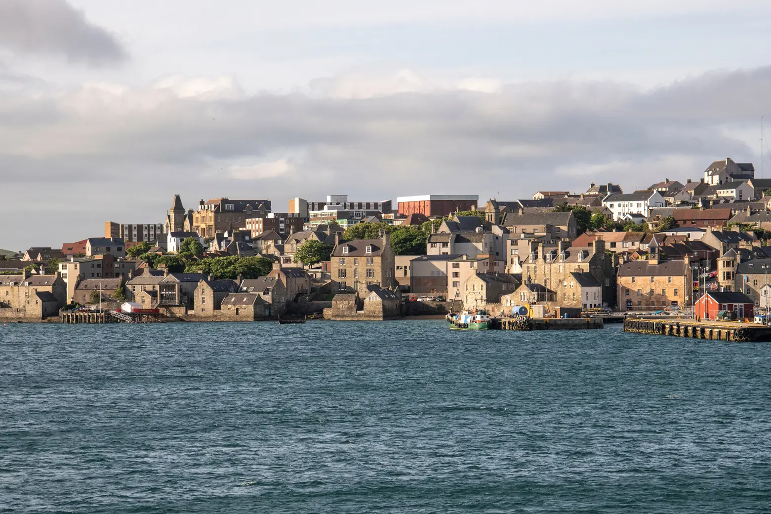 Coastal town with historic buildings on the waterfront under a cloudy sky.