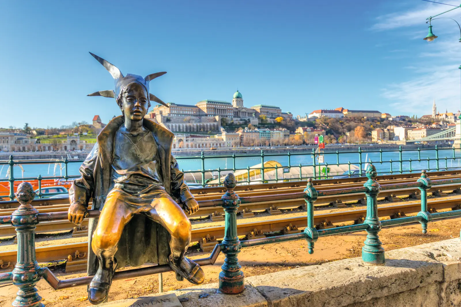 Statua in bronzo di una ragazza sulla riva del fiume, con Budapest sullo sfondo.