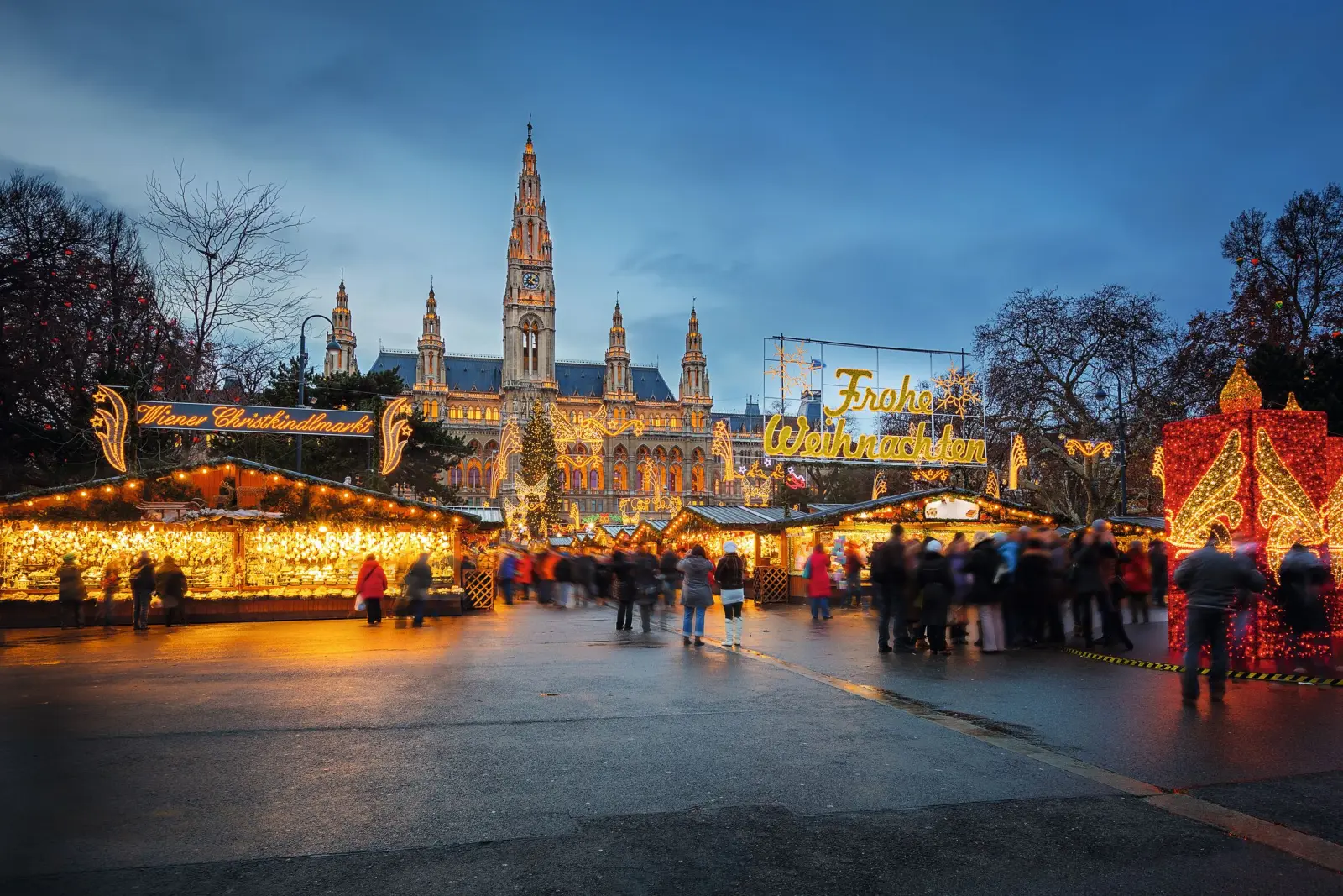 Wiener Weihnachtsmarkt am Abend mit beleuchteten Ständen und Rathaus im Hintergrund.