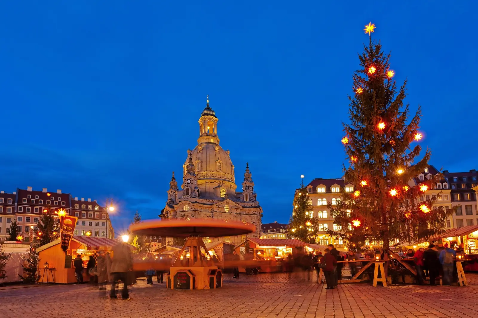 Marché de Noël en soirée devant une église historique avec un sapin de Noël illuminé
