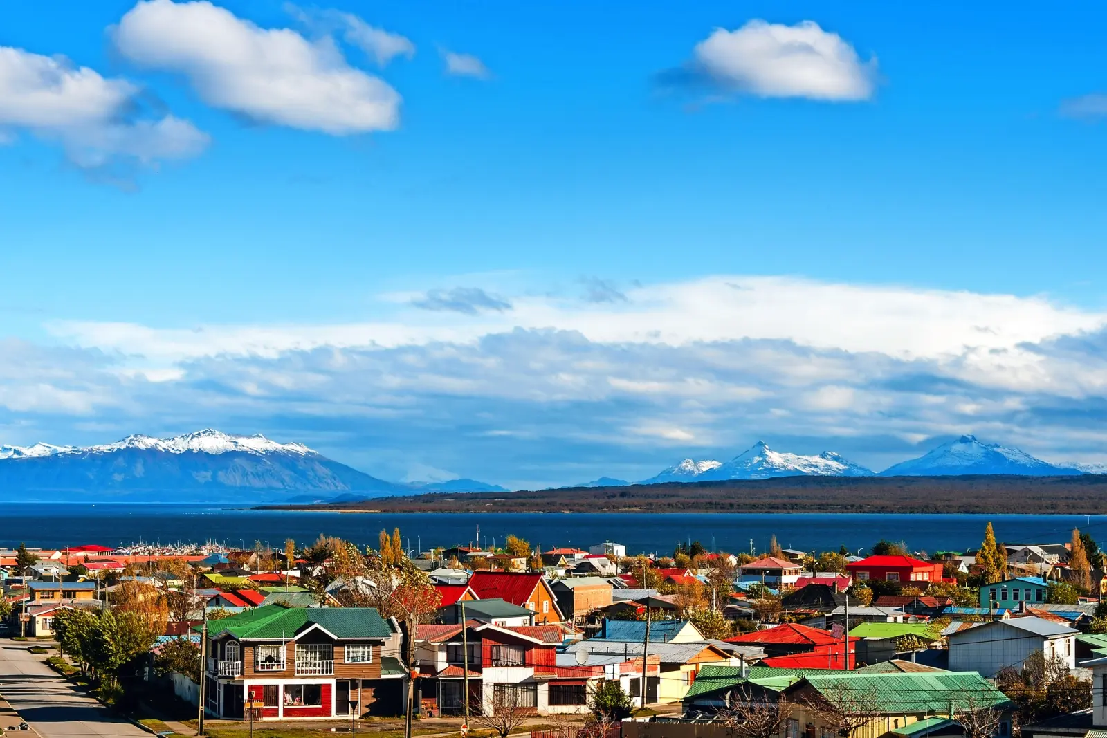 Cittadina con case colorate davanti a montagne innevate e cielo azzurro.