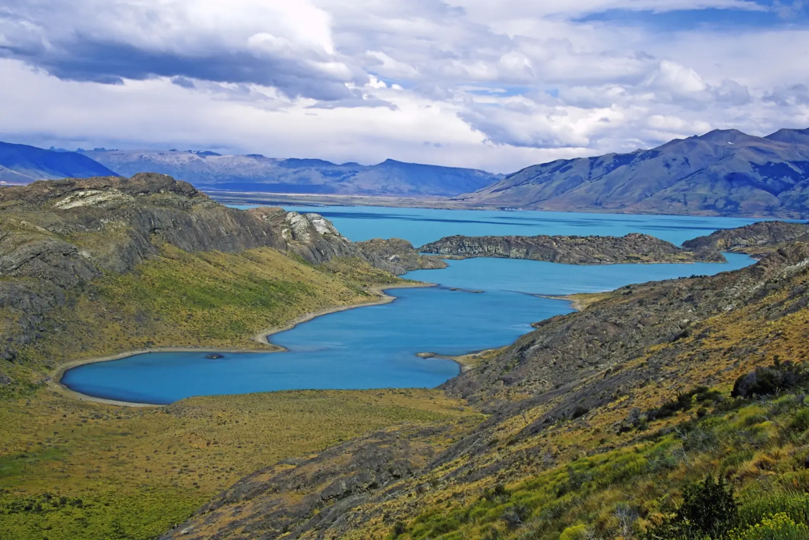 Vista su un paesaggio con lago azzurro e montagne circostanti sotto un cielo nuvoloso.