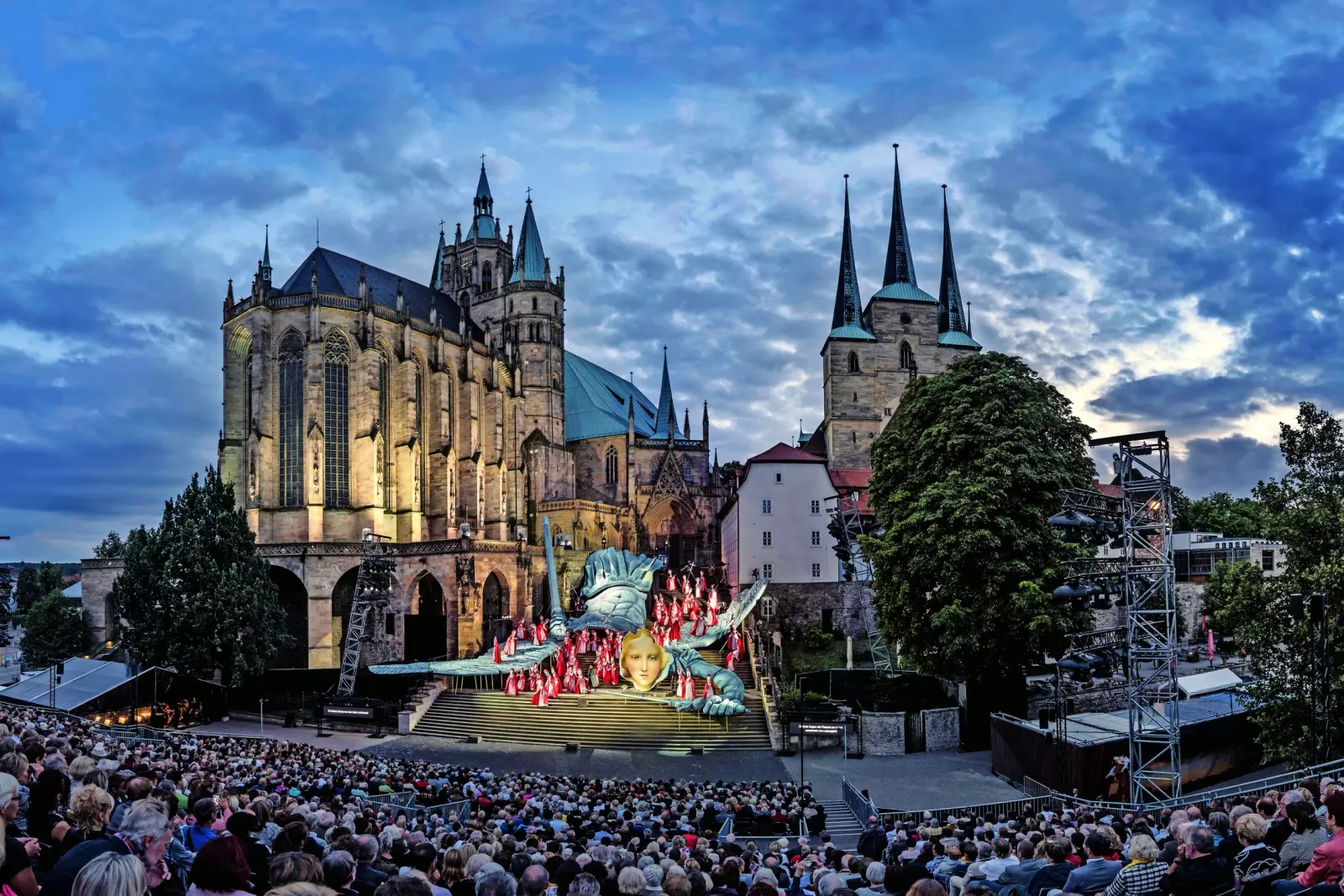 Représentation théâtrale en plein air devant une grande cathédrale gothique au crépuscule.