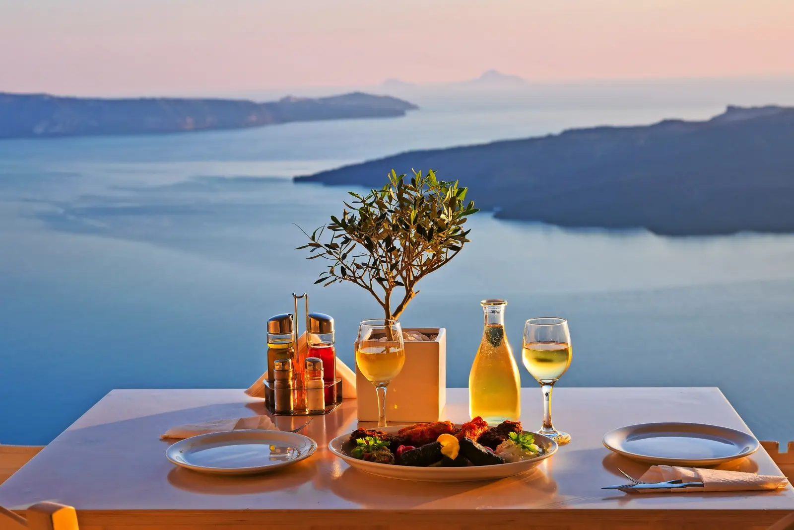 Table dressée pour le dîner avec du vin et vue sur la mer au coucher du soleil.