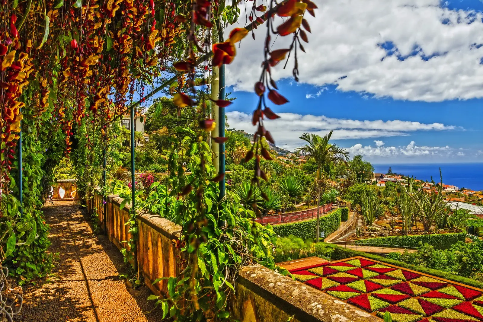 Garten mit farbigen Beeten und Meerblick unter bewölktem Himmel.