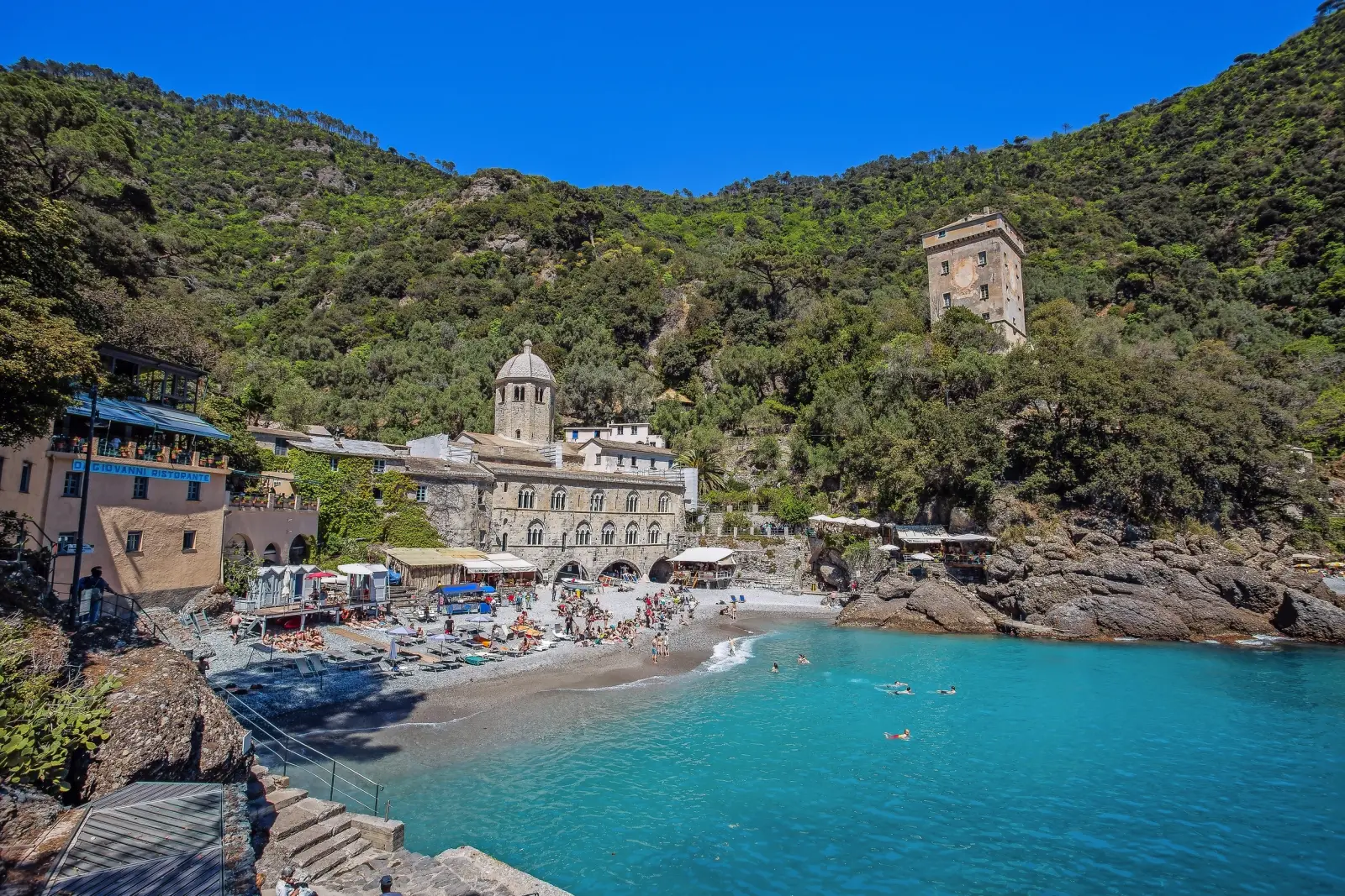 Spiaggia davanti a un complesso monastico con colline boscose sullo sfondo.