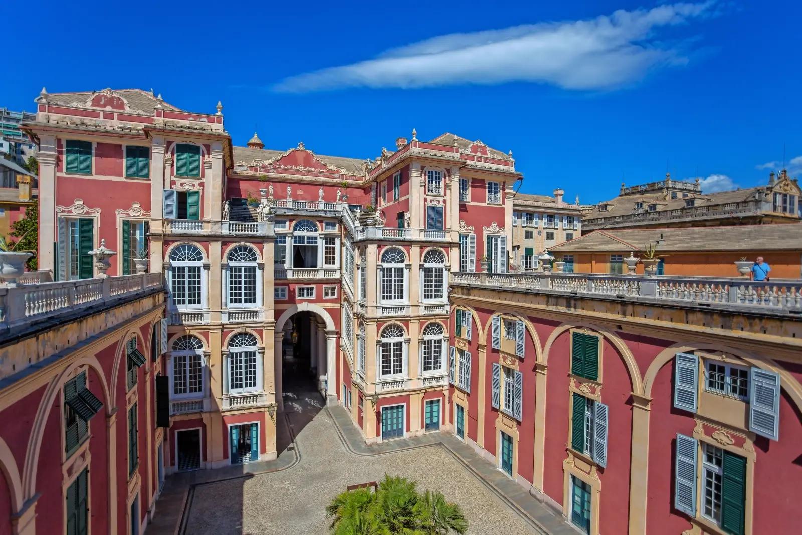 Edificio storico con facciata rosa e persiane blu sotto un cielo azzurro.
