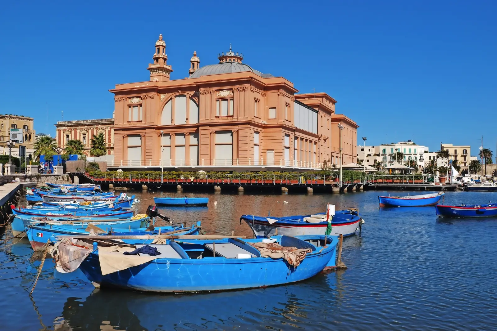 Several blue fishing boats in a harbour in front of a historic building.