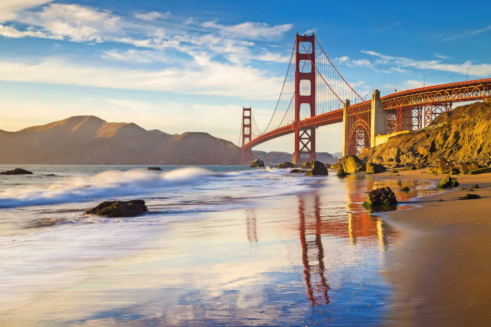 Golden Gate Bridge al tramonto con spiaggia e onde in primo piano.