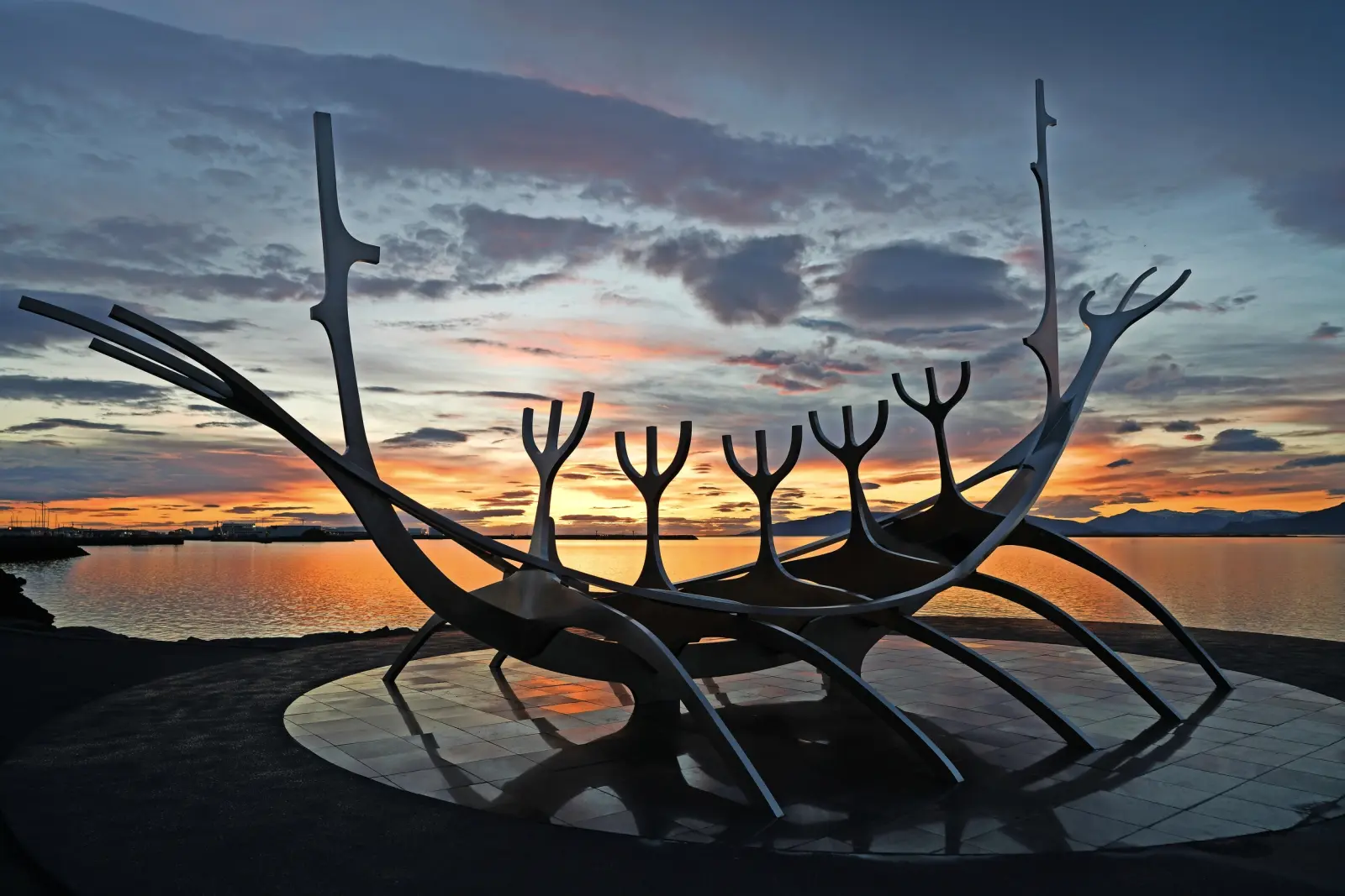 Viking ship sculpture against a colourful sunset by the water.