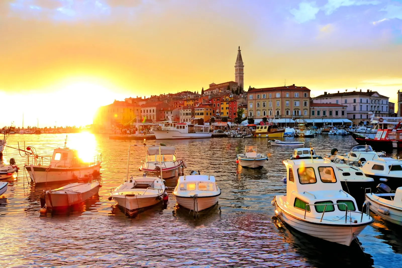 Boote in einem Hafen bei Sonnenuntergang mit einer Altstadt im Hintergrund.