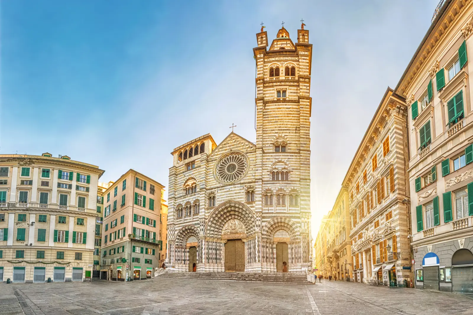 Cattedrale storica a strisce bianche e grigie su una piazza vuota al tramonto.