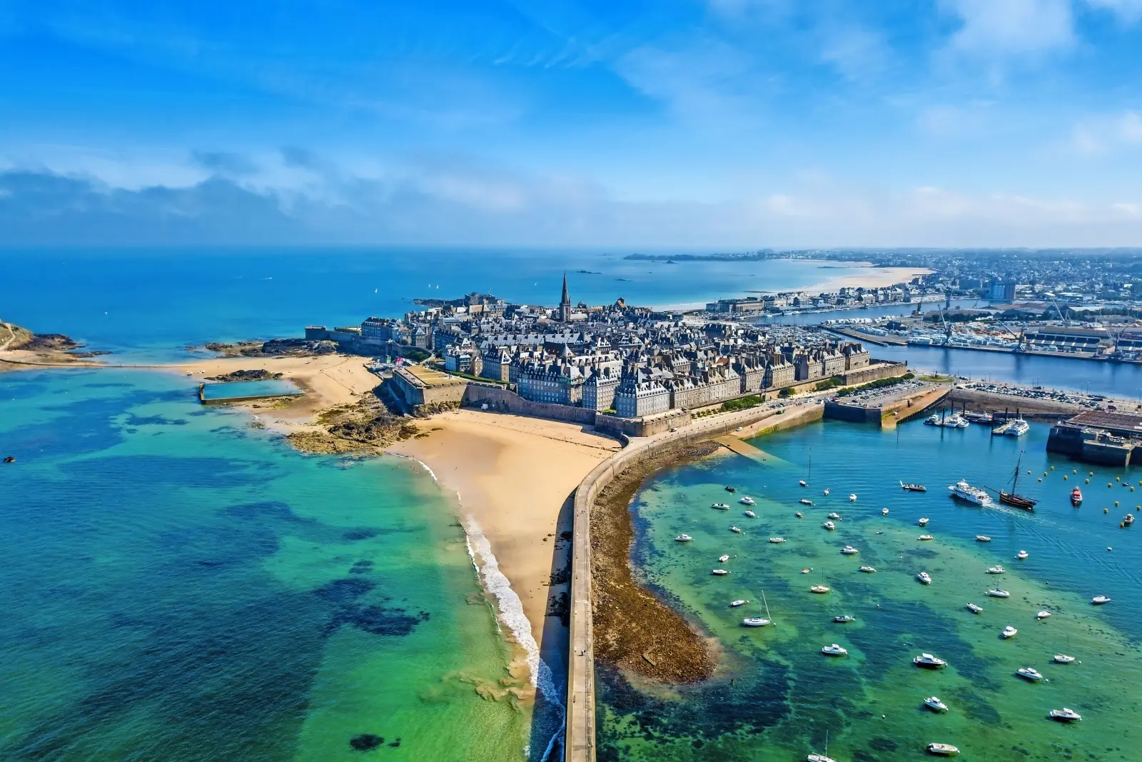 Coastal town with historic buildings and a harbour, surrounded by turquoise water.