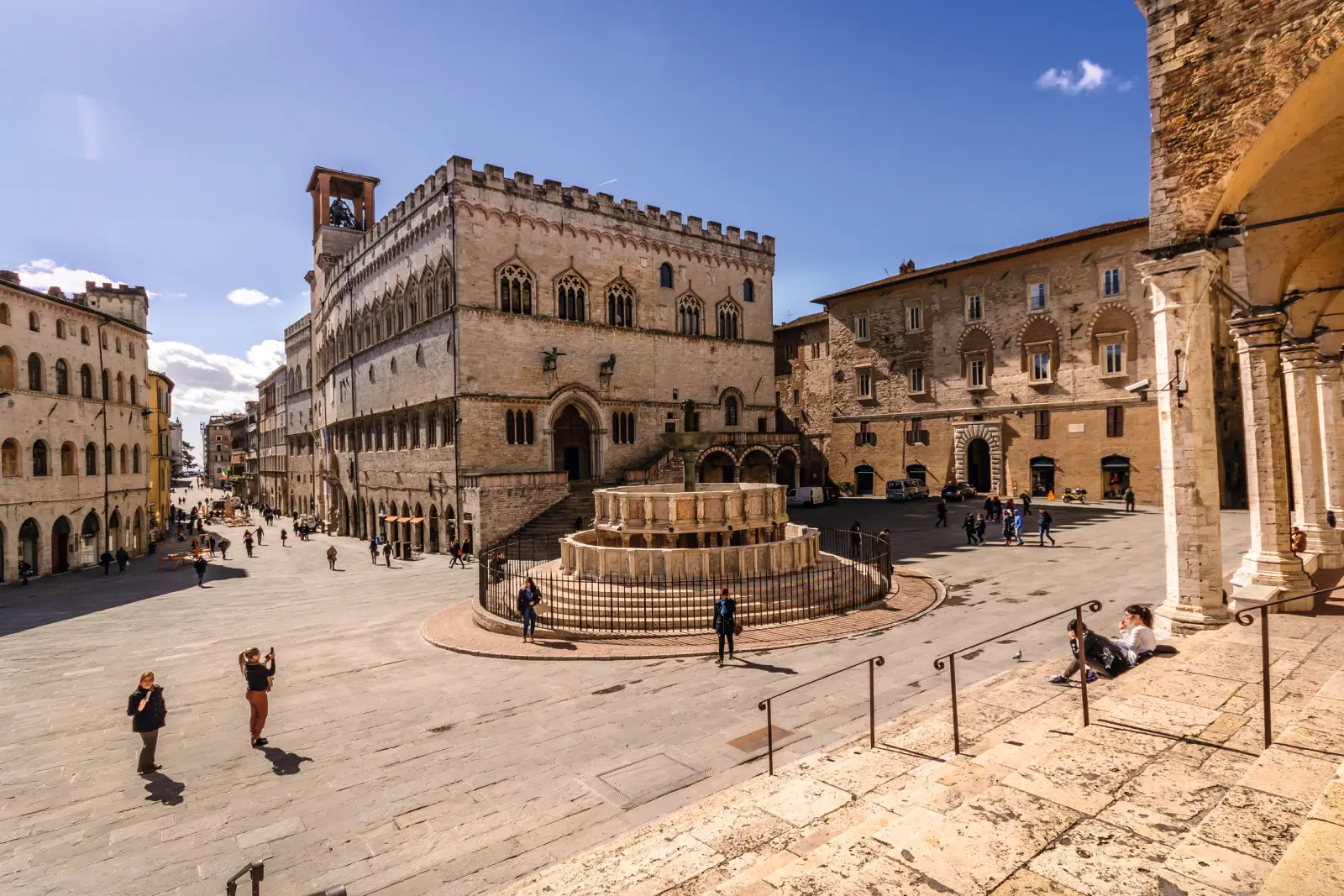 Piazza storica con fontana in una città soleggiata.