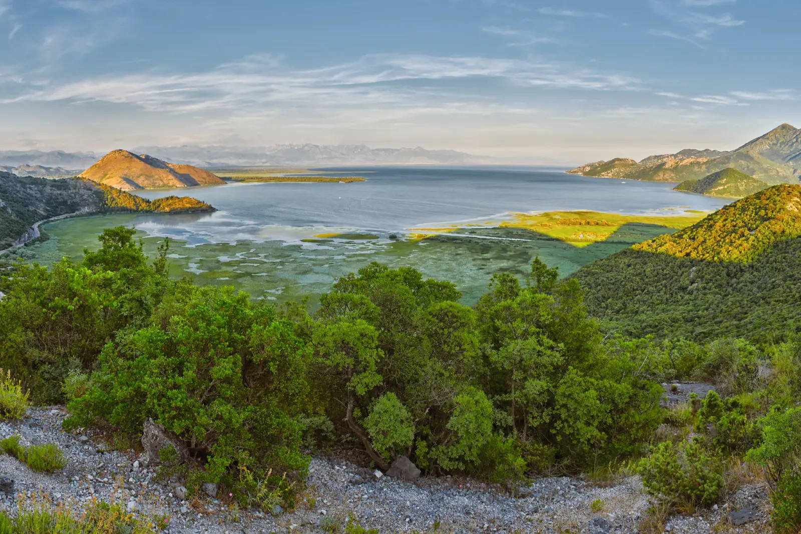 Panorama di un lago con colline verdi circostanti e cielo azzurro.