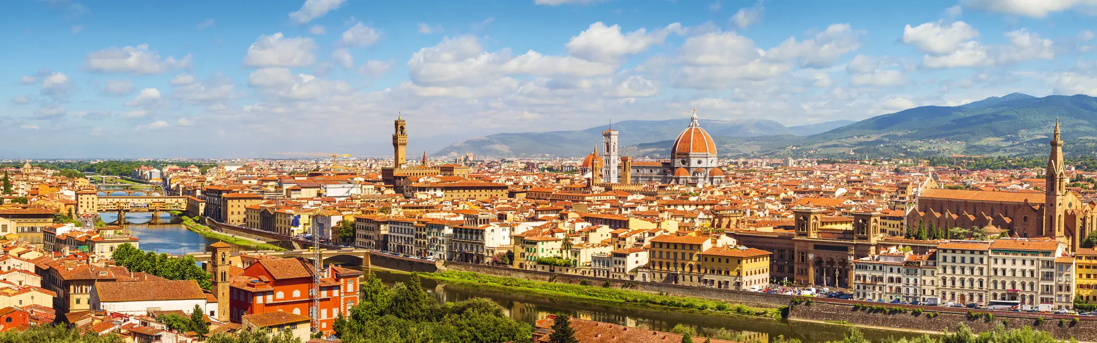 Panoramic view over Florence with the cathedral dome and the River Arno under a blue sky.