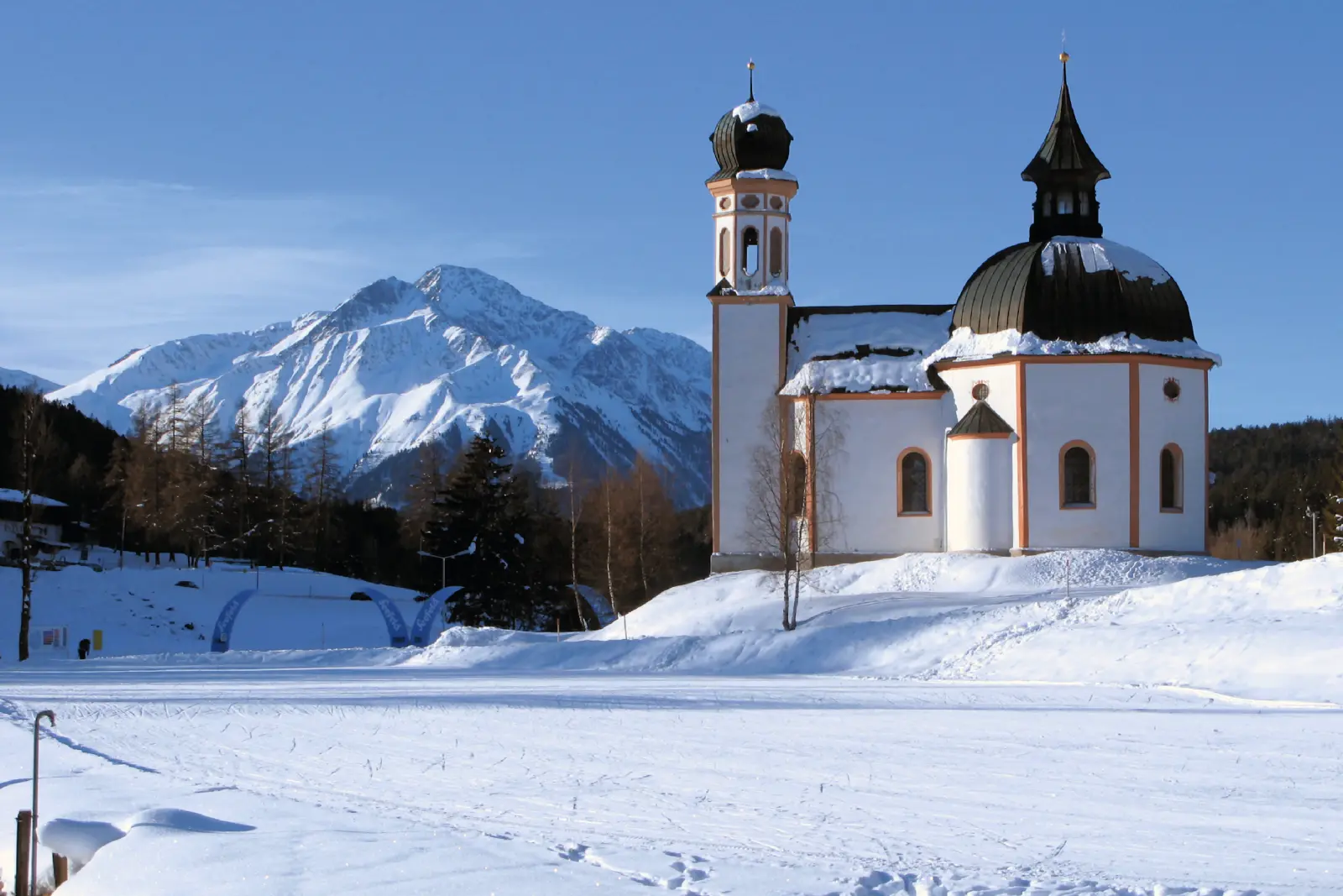Église dans un paysage alpin enneigé avec des montagnes à l’arrière-plan.