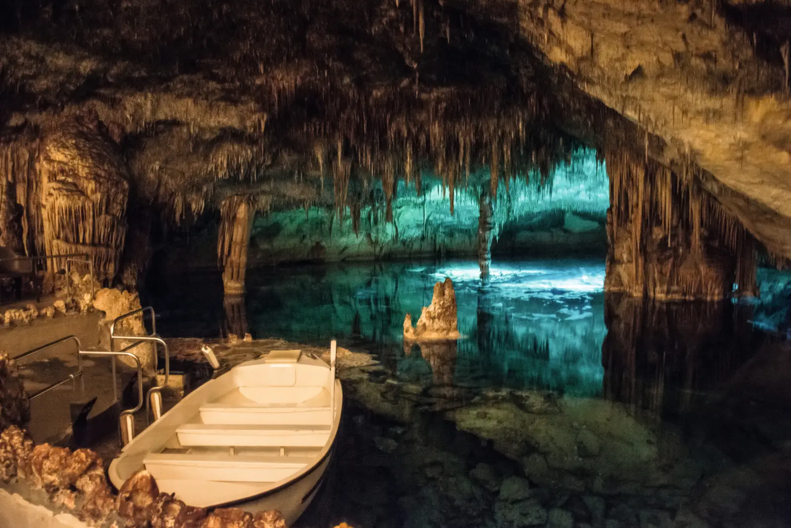 Barca in una grotta illuminata con stalagmiti e stalattiti.