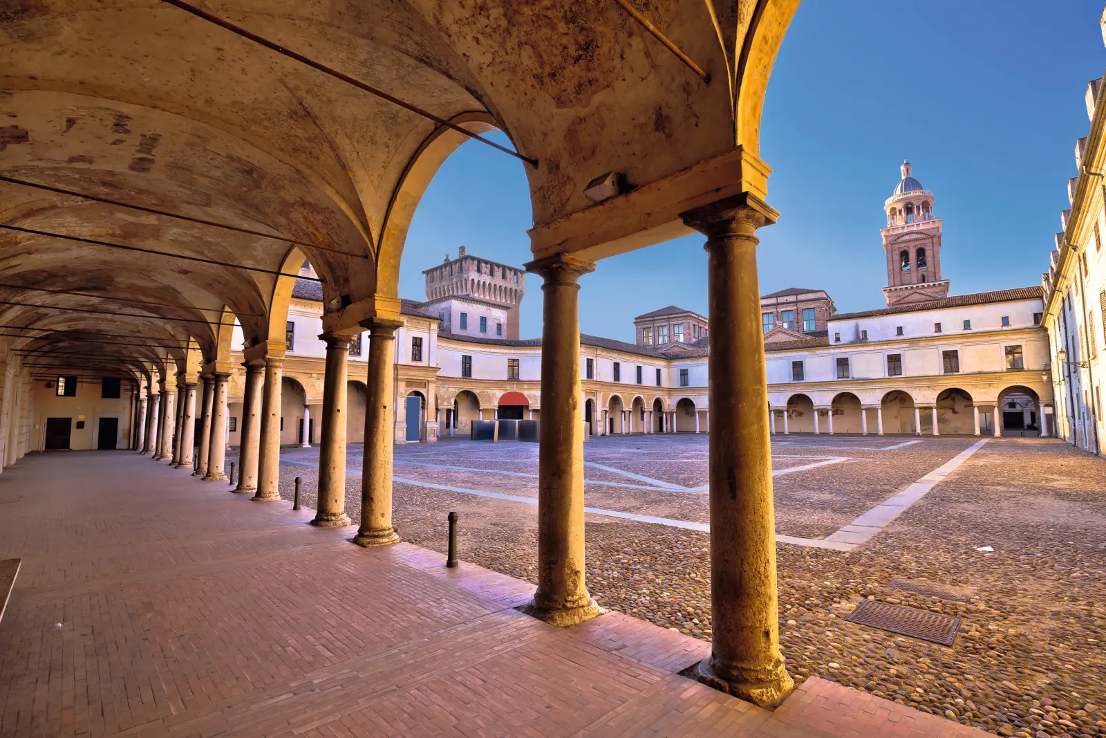 Historic arcaded courtyard with a bell tower under a blue sky.