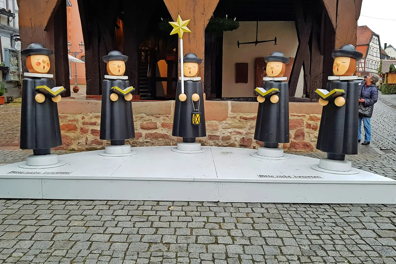 Holzfiguren von Kurrendesängern auf einem Marktplatz.