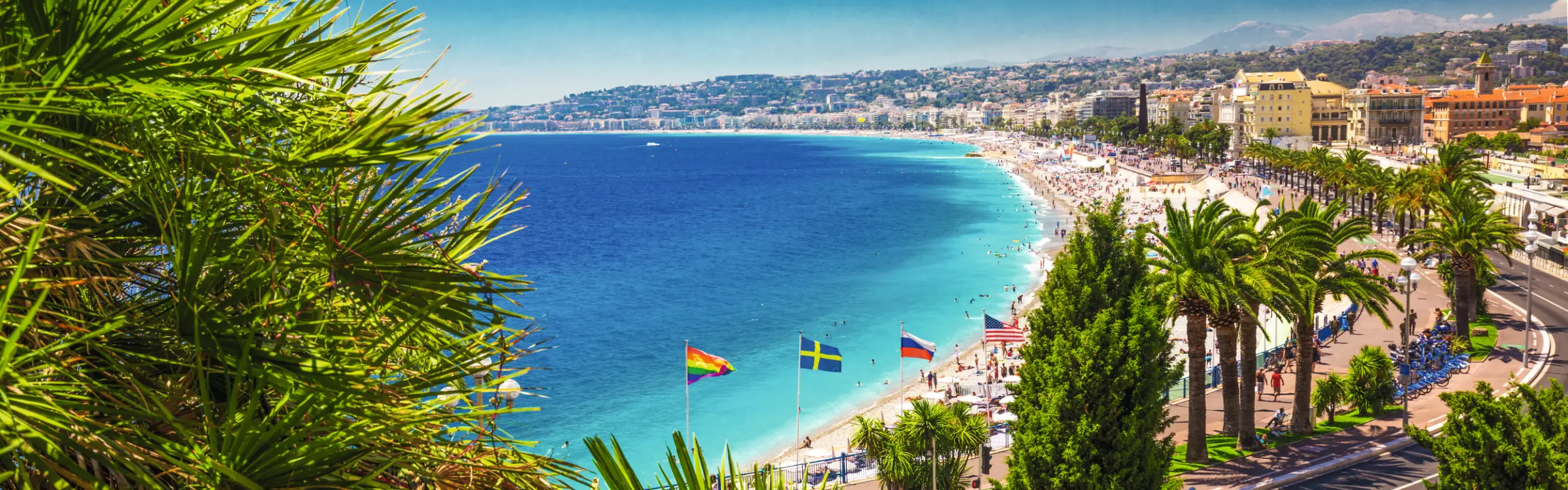Veduta di una città costiera con spiaggia, palme e mare blu.