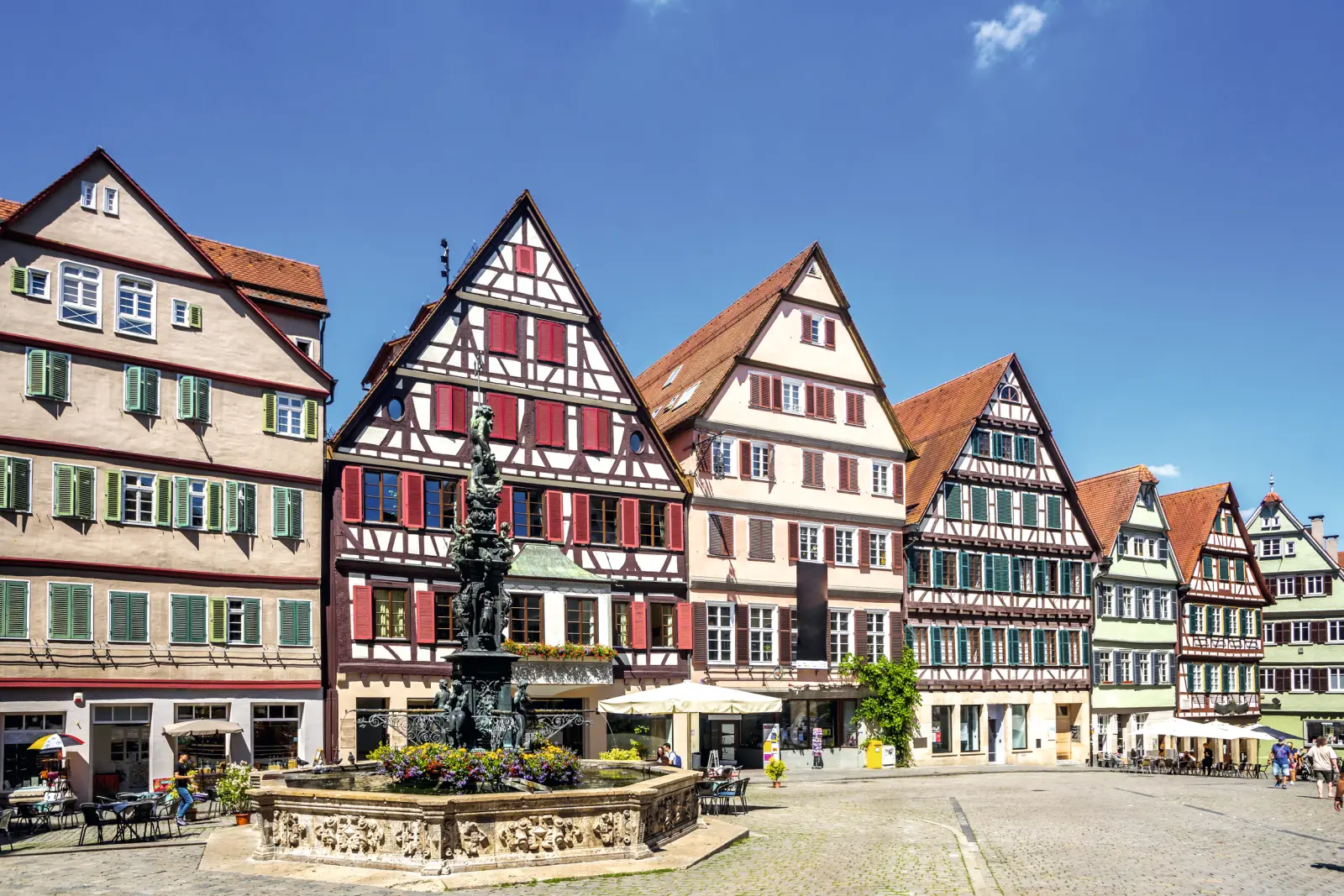 Half-timbered houses in a historic old town, with a fountain in the foreground.