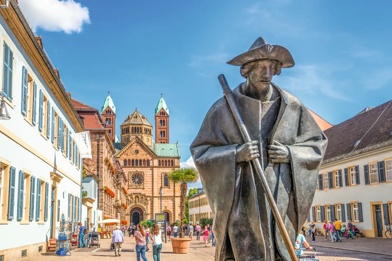 Statue d’un pèlerin devant la cathédrale de Spire, dans une zone piétonne animée.