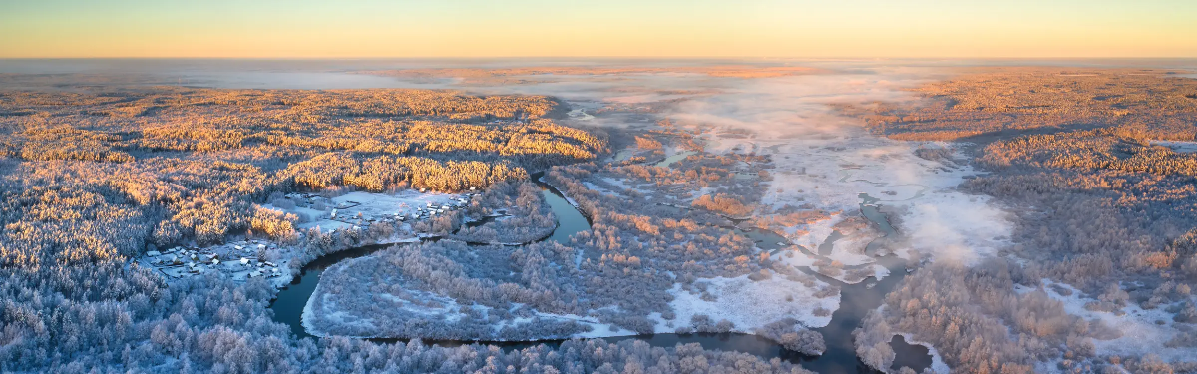 Snowy landscape with river seen from above at sunrise.