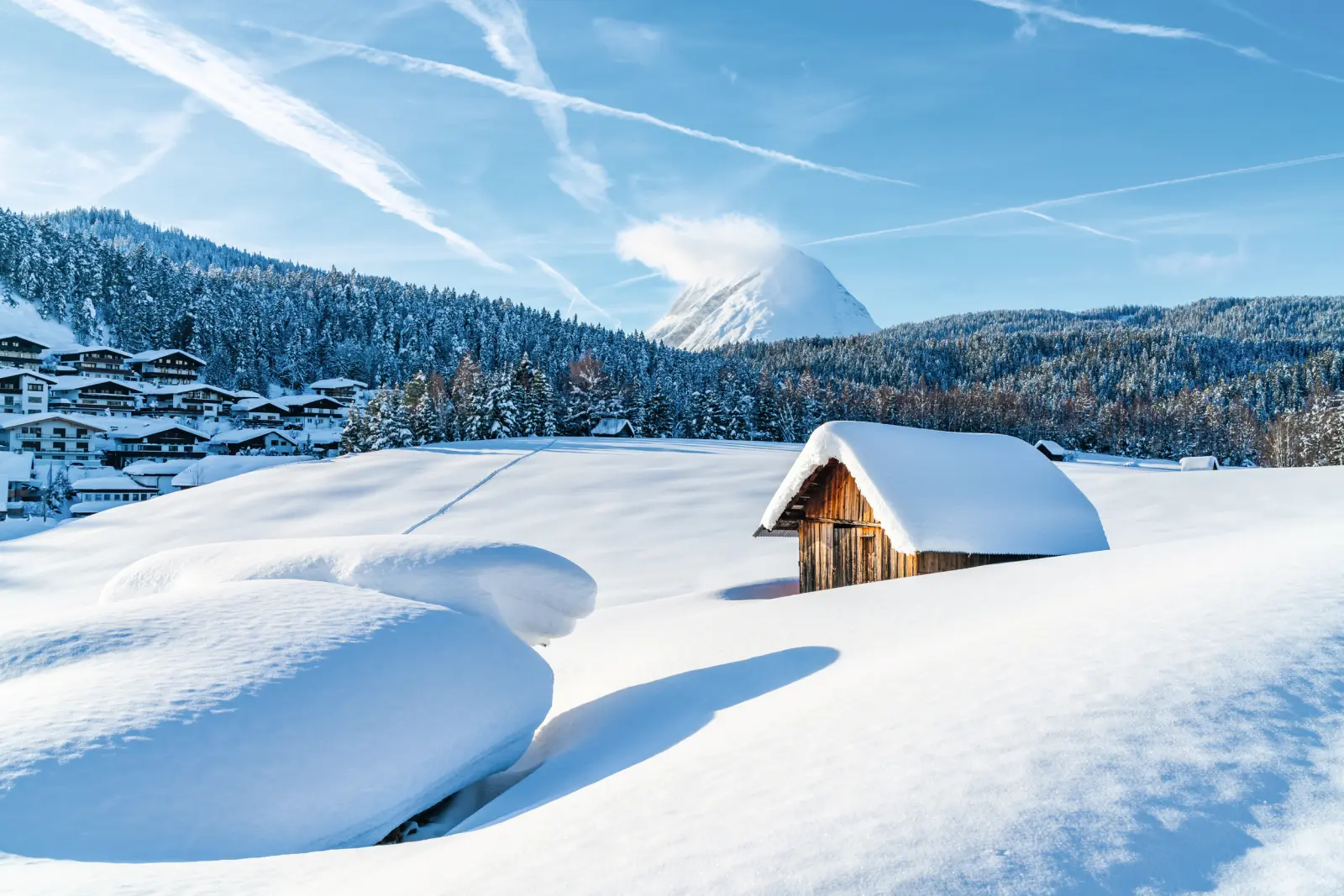 Paysage enneigé avec chalet et montagnes à l’arrière-plan sous un ciel bleu.