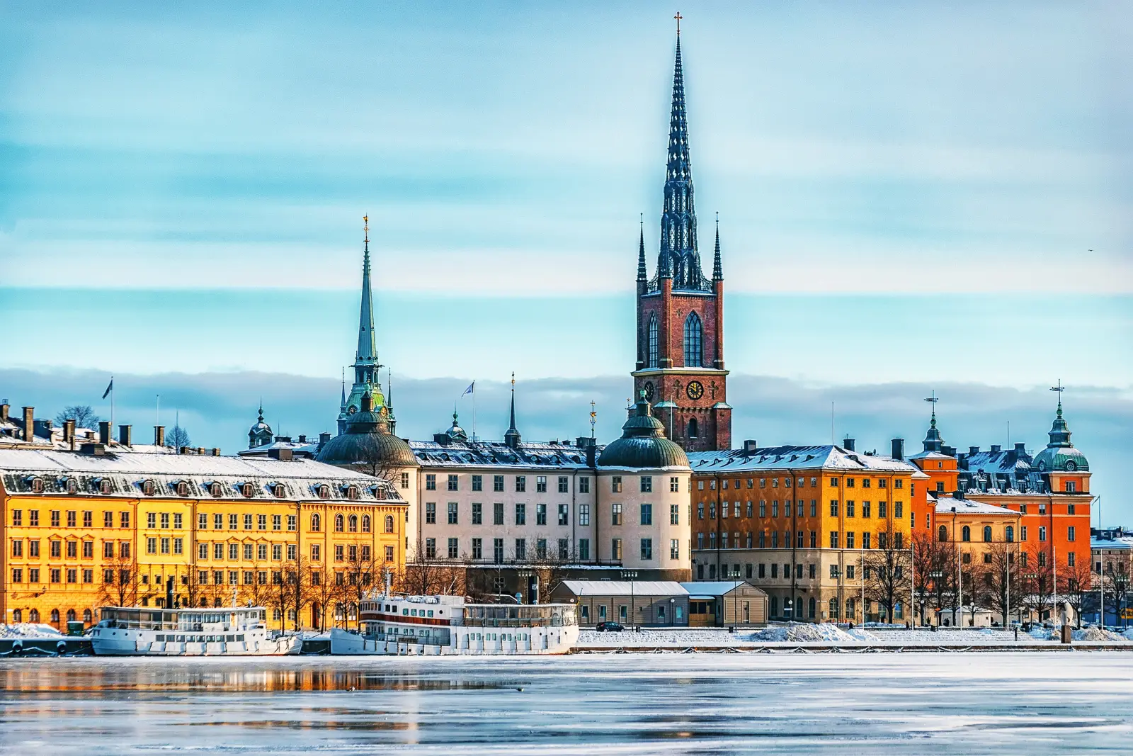 Veduta di una città innevata con case colorate e campanili sull'acqua.