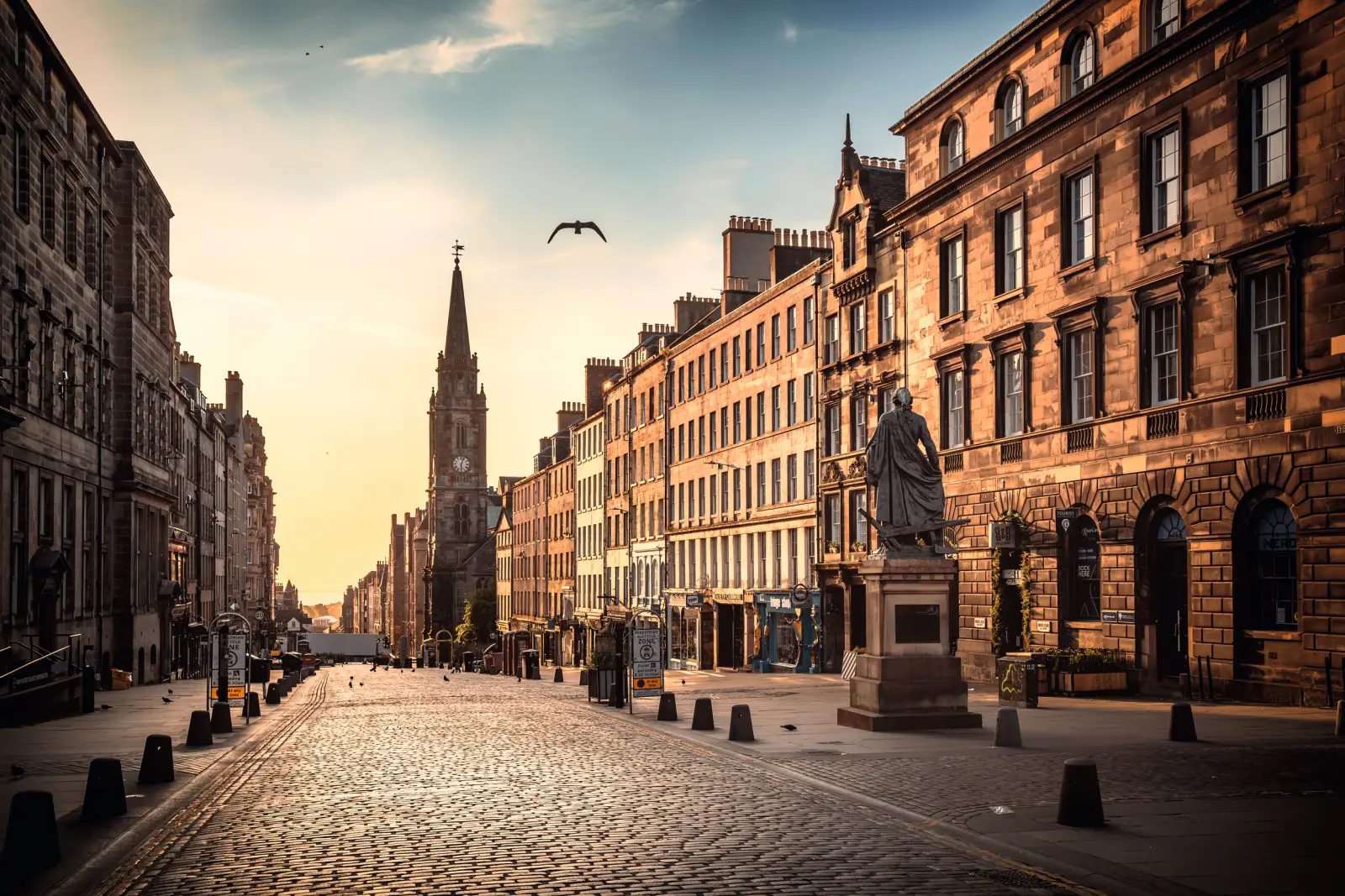 Cobbled street with historic buildings and a church in the background at sunset.