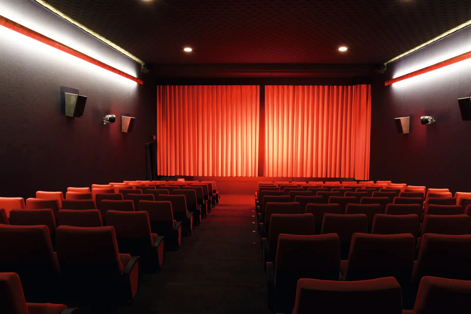 Cinema auditorium with empty red seats and a bright red curtain.
