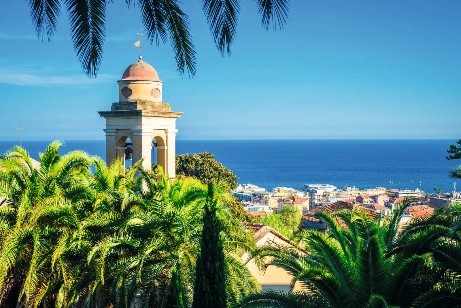 Bell tower in front of the backdrop of Sanremo on the Ligurian coast, with sea views and palm trees.