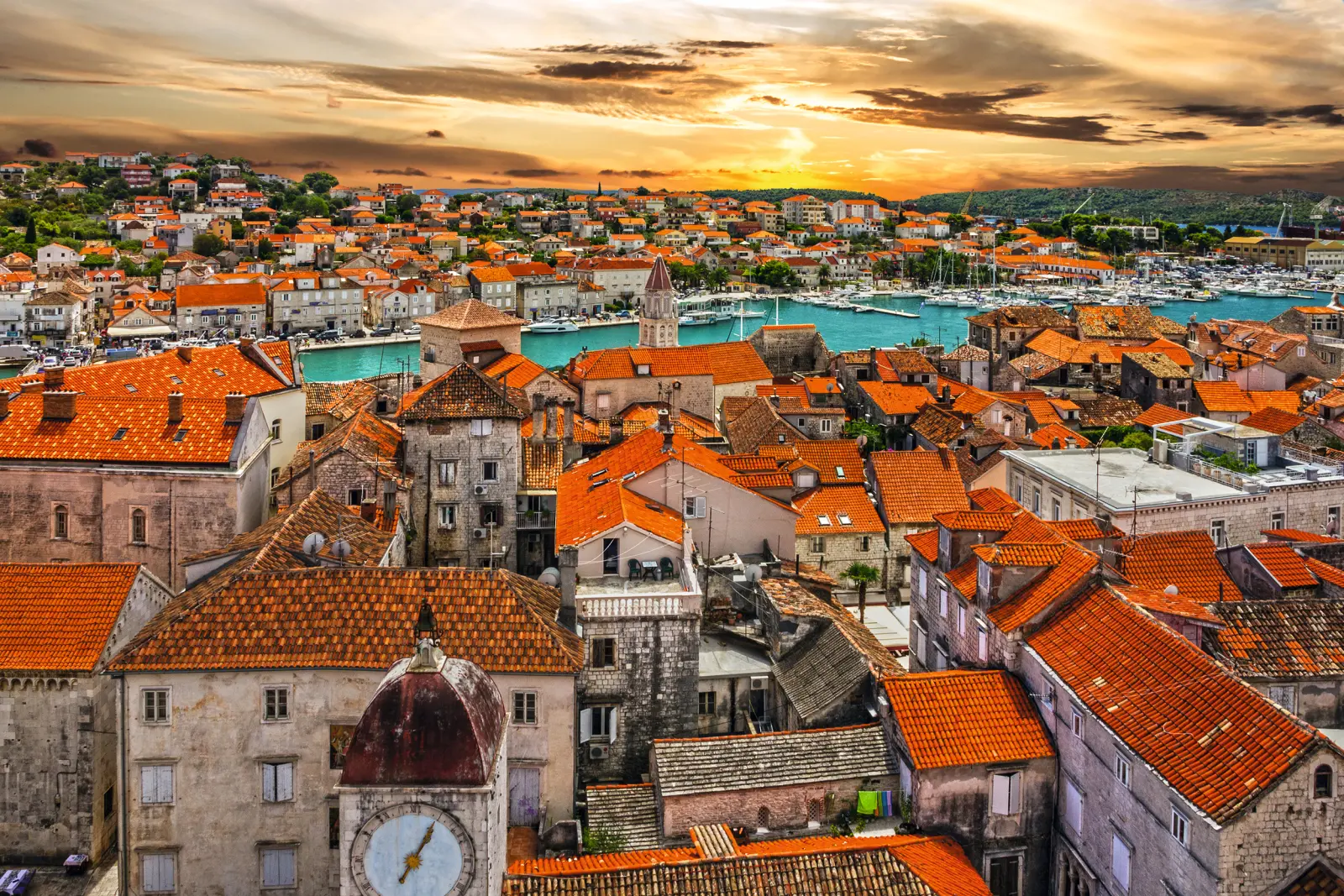 Stadtansicht von Trogir bei Sonnenuntergang mit roten Dächern und Wasser im Hintergrund.