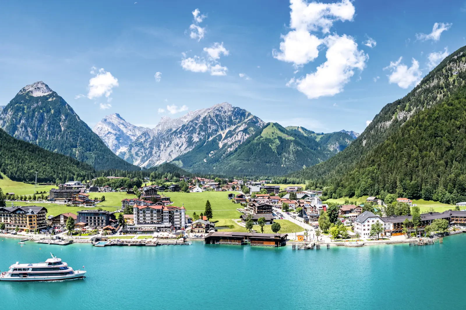 Szenische Ansicht eines Sees mit Bergen, Dorf und einem Boot bei klarem Himmel.