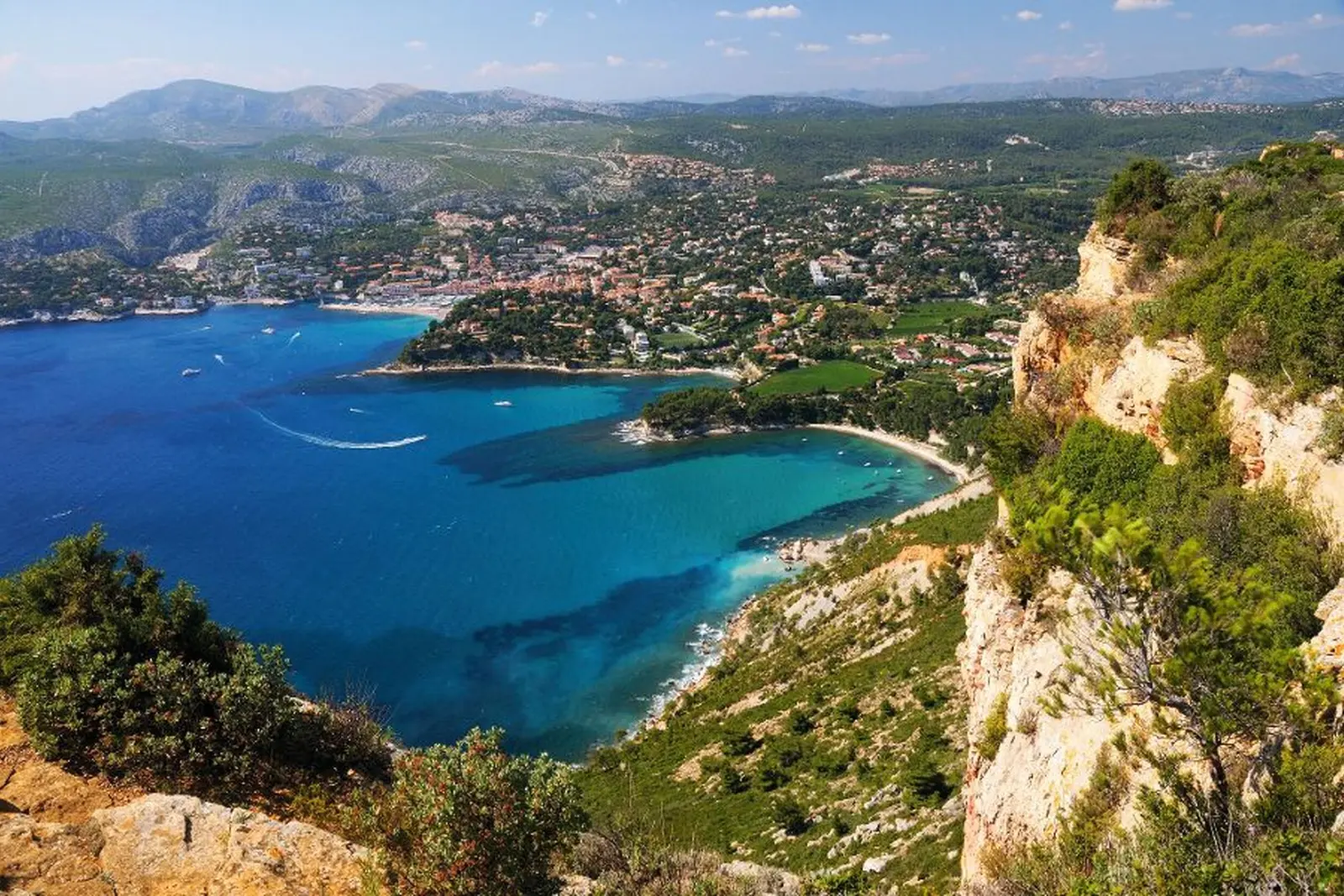 Paesaggio costiero con mare e scogliere, città sullo sfondo, cielo azzurro.