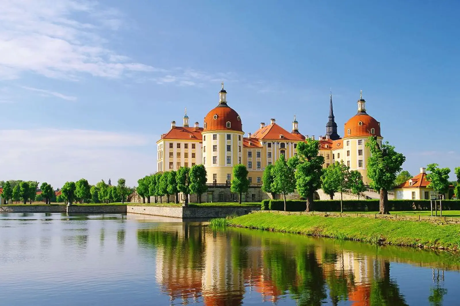 Schloss mit roten Kuppeln und Türmen an einem sonnigen Tag, umgeben von Wasser und Bäumen.