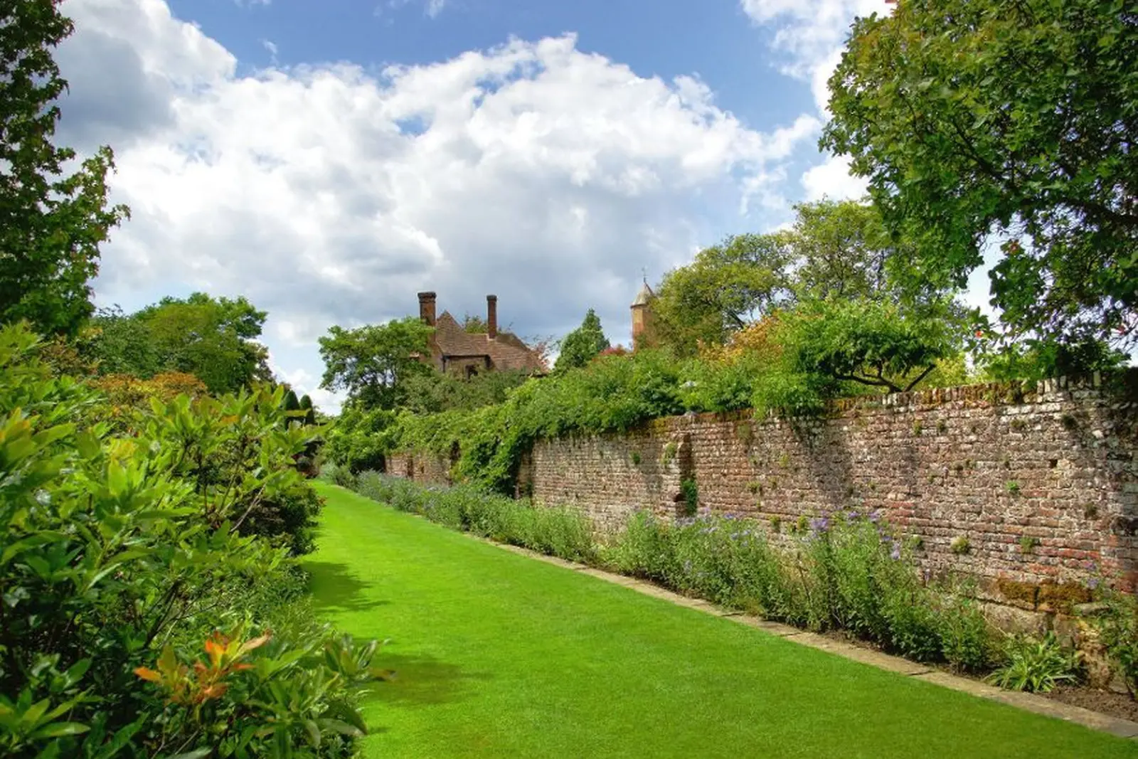 Well-kept garden with brick wall and historic house in the background.
