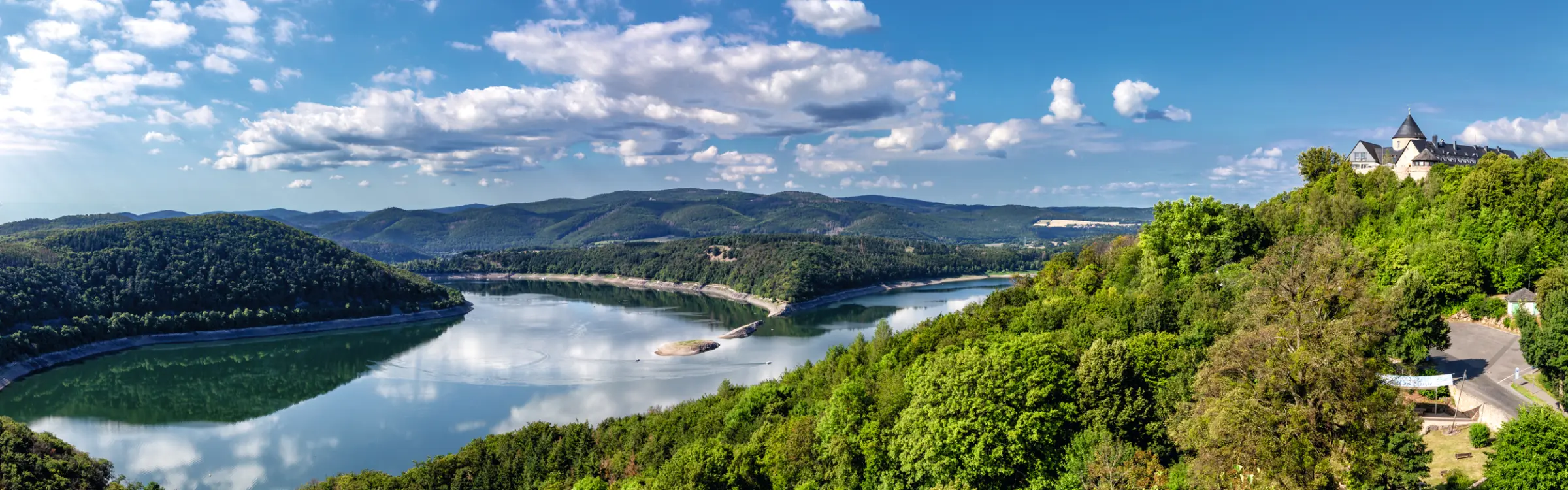 Panorama d'un paysage fluvial avec des collines boisées et un château.