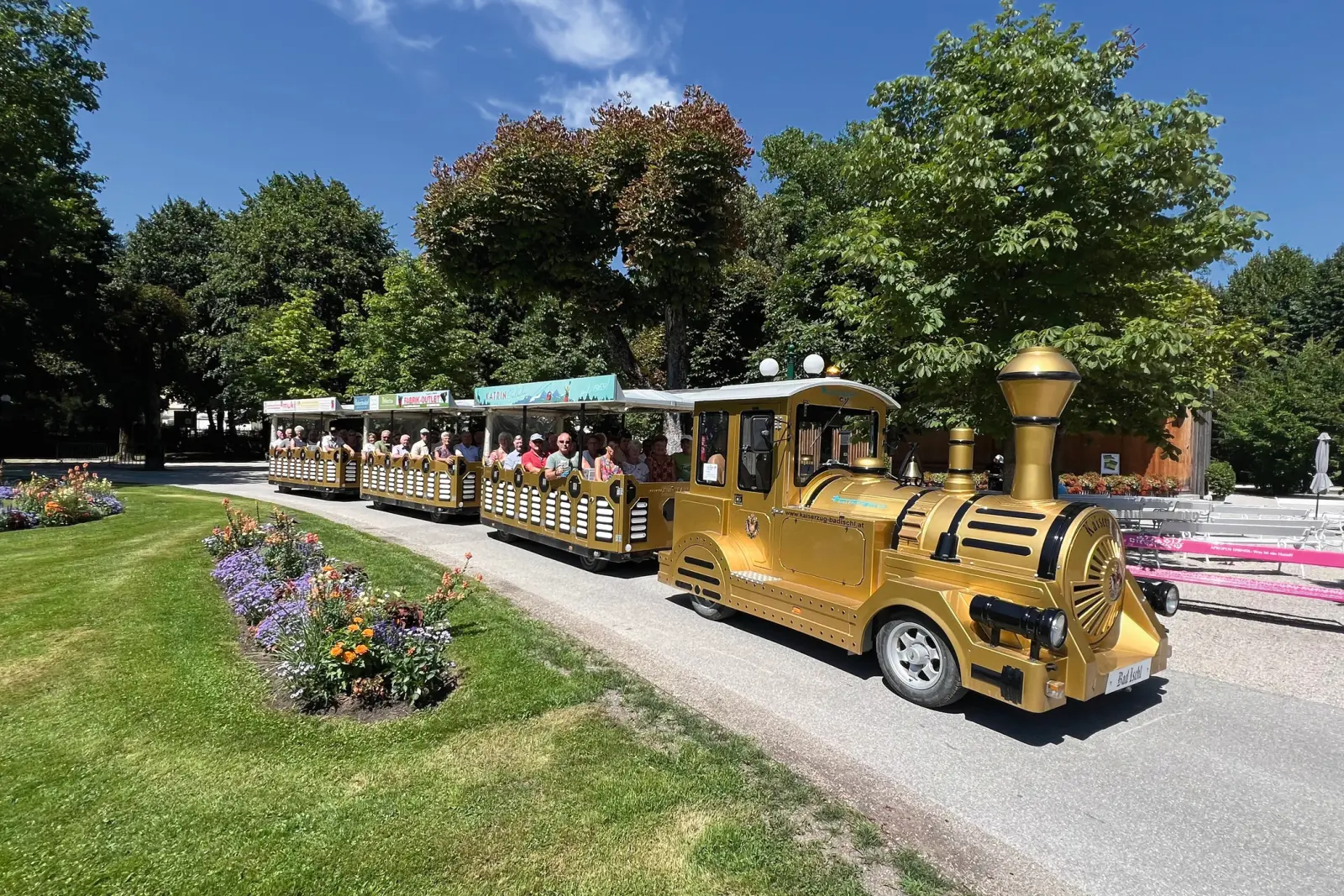 Petit train touristique doré traversant un parc par temps ensoleillé.