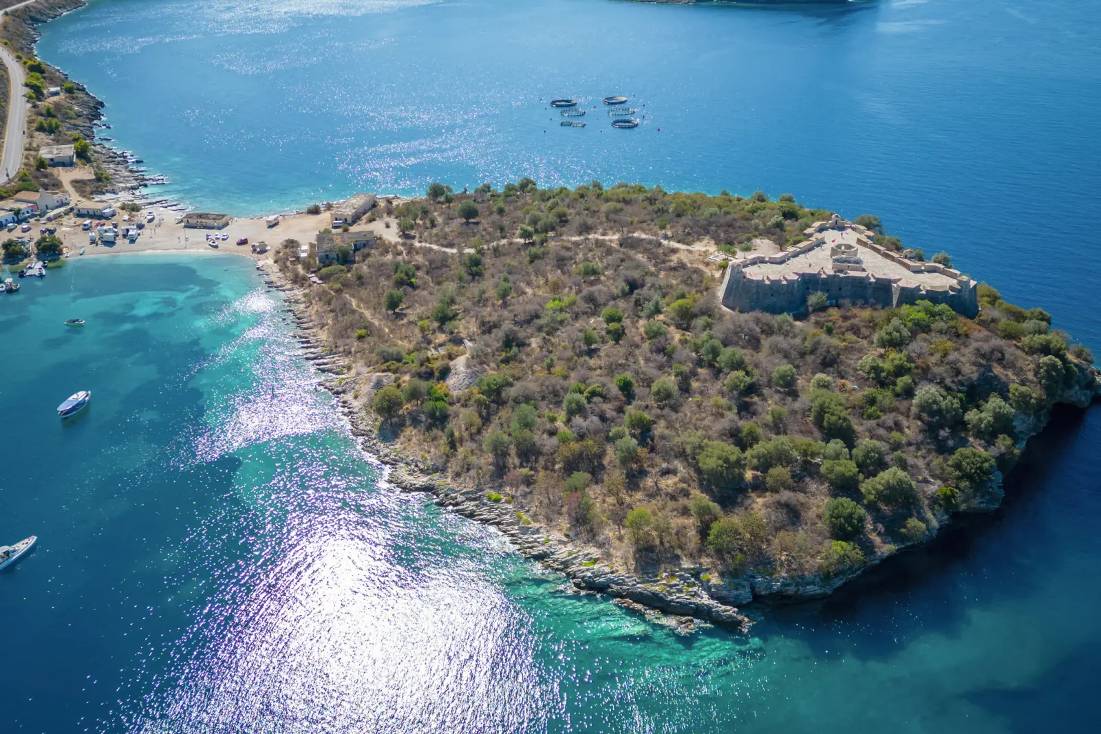Veduta aerea di una penisola ricoperta di vegetazione nel mare blu con piccole barche.