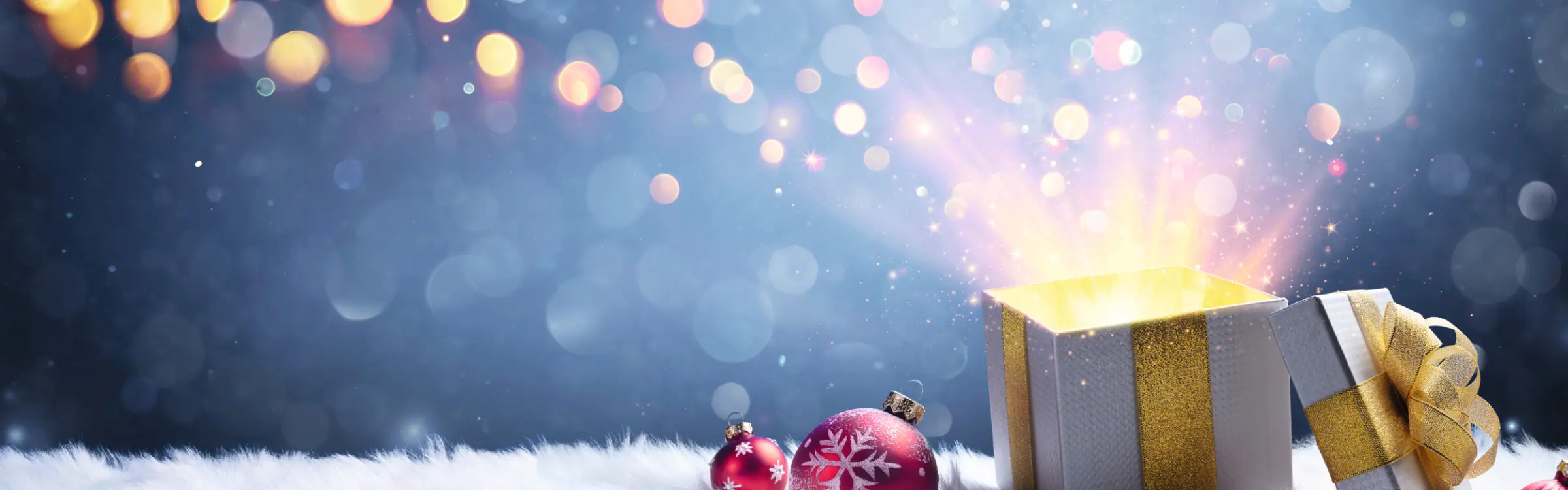 Offene Geschenkbox mit leuchtendem Inhalt neben Weihnachtsschmuck auf Schneedecke