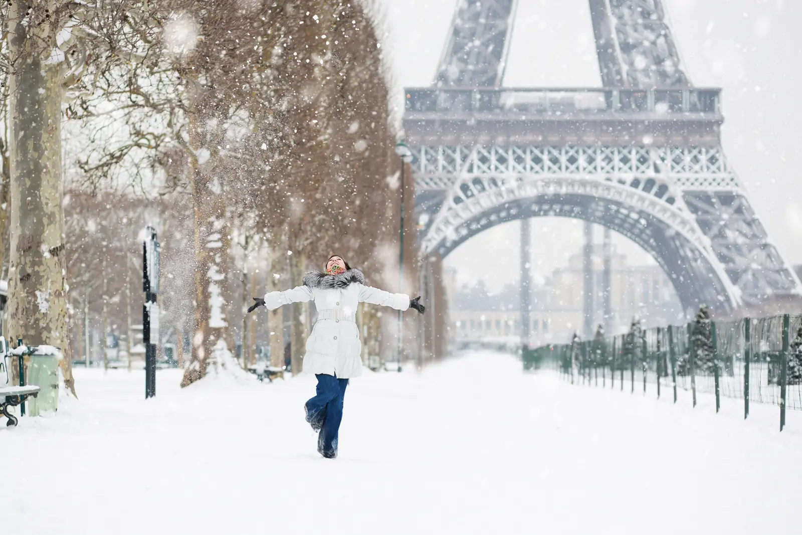 Una persona in piedi con le braccia aperte nella neve davanti alla Torre Eiffel di Parigi, in inverno.