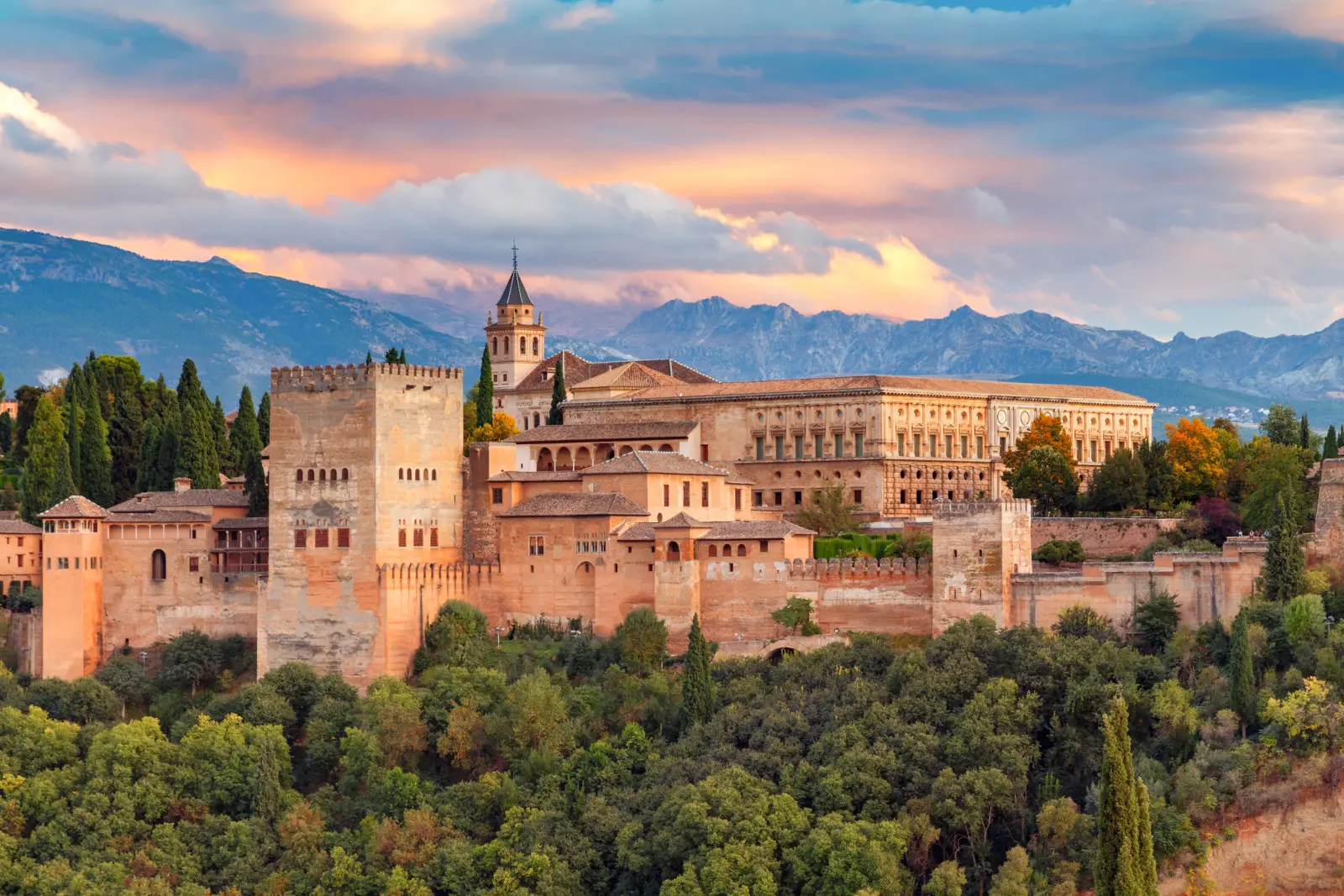 Blick auf die Alhambra in Granada bei Sonnenuntergang mit Bergen im Hintergrund.