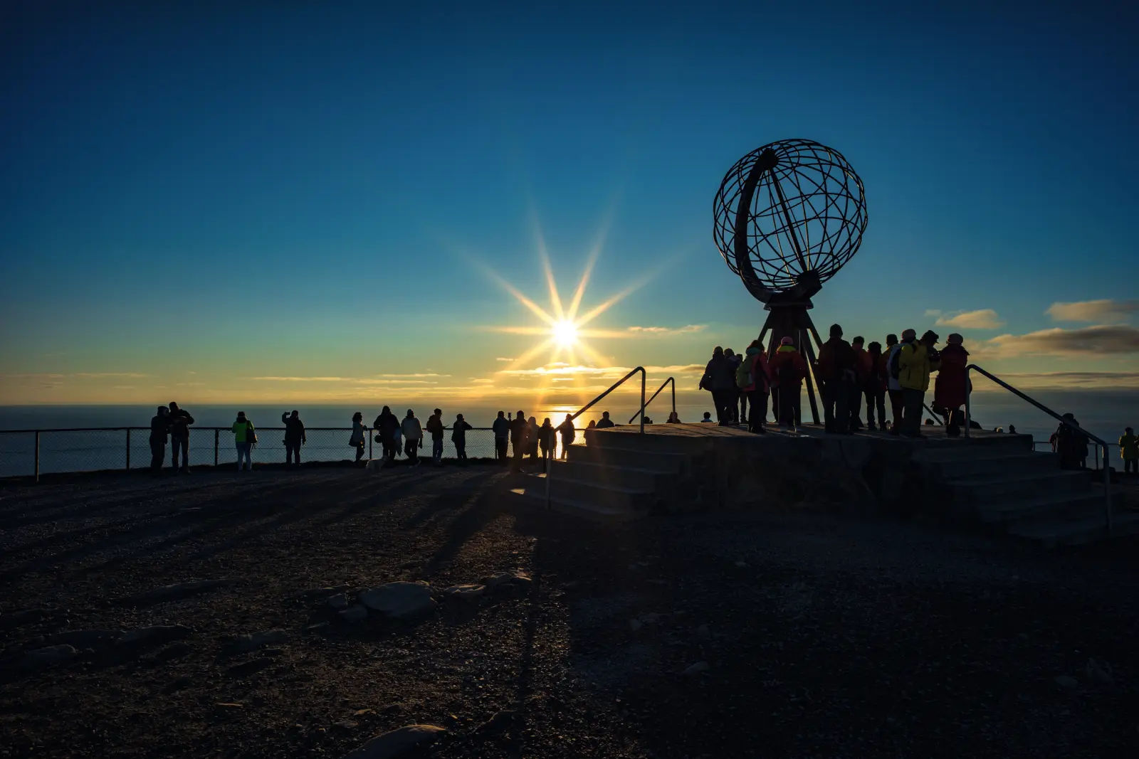 Persone al tramonto a Capo Nord con la scultura del globo.
